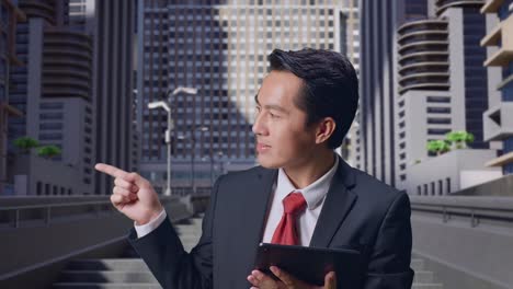 an asian business man using tablet and pointing to the side in city