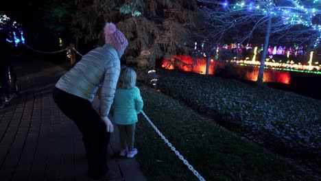 mother and daughter looking at christmas decorations of colorful lights in a park