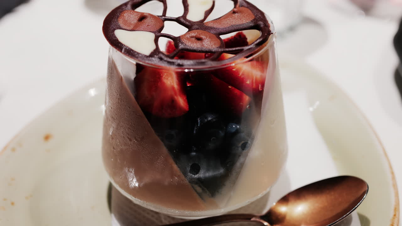 Elegant dessert in a glass topped with fresh strawberries, blueberries, and a chocolate lattice decoration