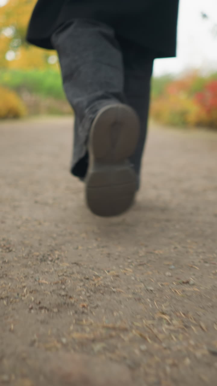 primer plano de piernas caminando en un jardín durante el otoño, con pantalones vaqueros negros y zapatos de lona, capturando la esencia de un paseo tranquilo entre las hojas de otoño