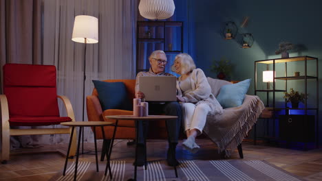 happy senior old couple using laptop pc talking reading discussing internet computer news at home