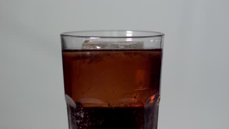 Cola-in-Drinking-Glass-with-Bubbles-and-Big-Ice-Cube-on-Grey-Background-Close-up