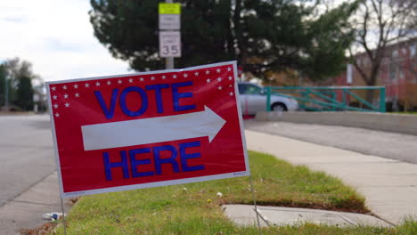 vote here sign pointing right with person driving car past and walking in background, close up