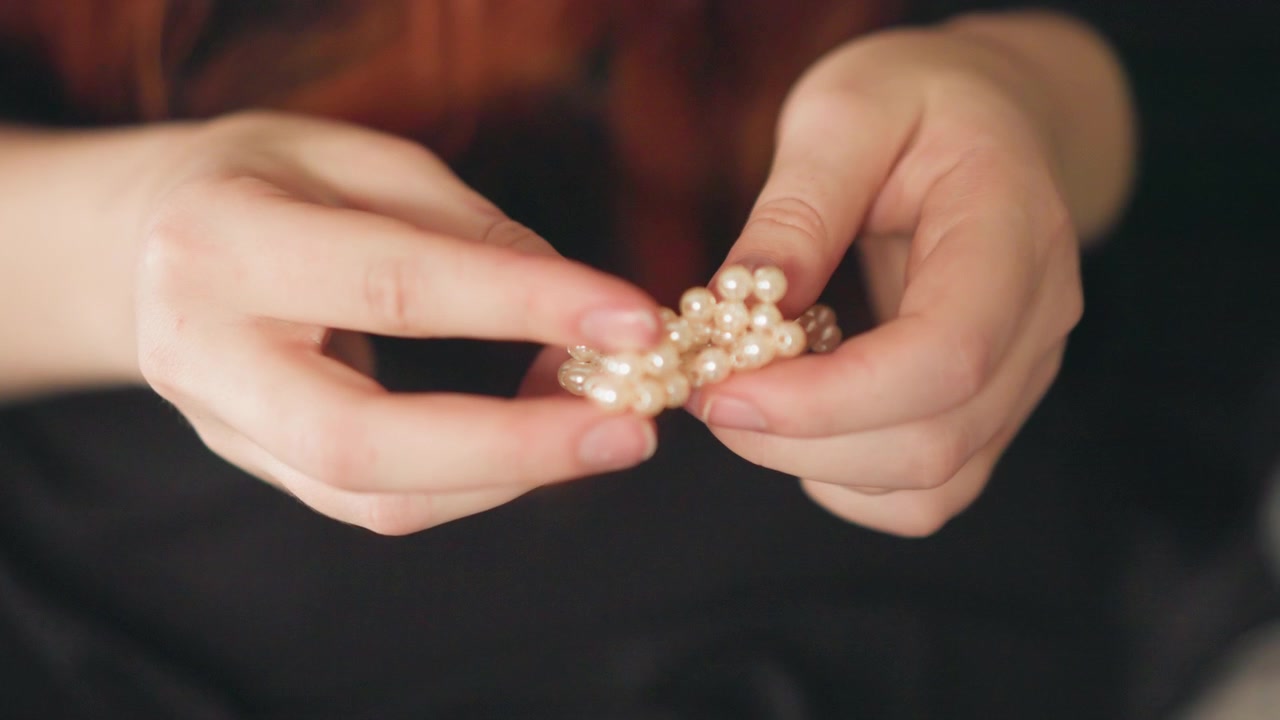 Primo piano di mani che tengono perle, una chiromante conta e gira delicatamente gioielli di famiglia. Una luce calda e morbida e una profondità di campo ridotta creano un'atmosfera intima e contemplativa, con dita delicate e un tocco sottile.