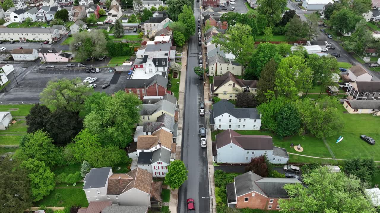 Red car driving on straight street in american neighborhood. Aerial birds eye shot. Cloudy spring day in american town. Green trees blossoming in spring. tracking shot. PA, United States.