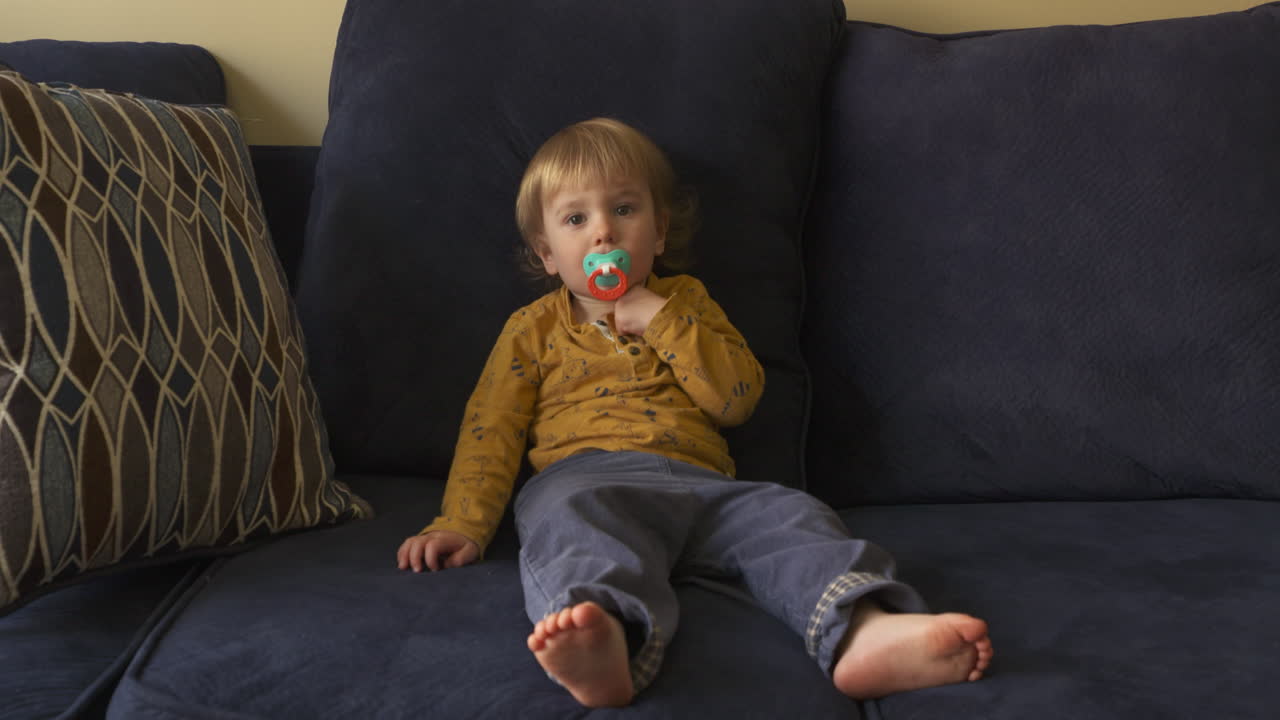 Toddler boy sitting on a sofa sucking on a pacifier