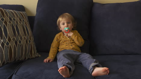 niño pequeño sentado en un sofá chupando un chupete