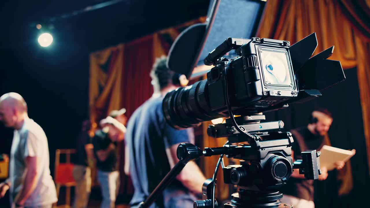 Close-up of a professional video camera on a film set, capturing a behind-the-scenes look with crew
