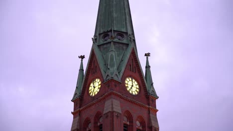 tower of christian trinity church in arendal norway - static evening shot with birds flying around uplit clock and sky background