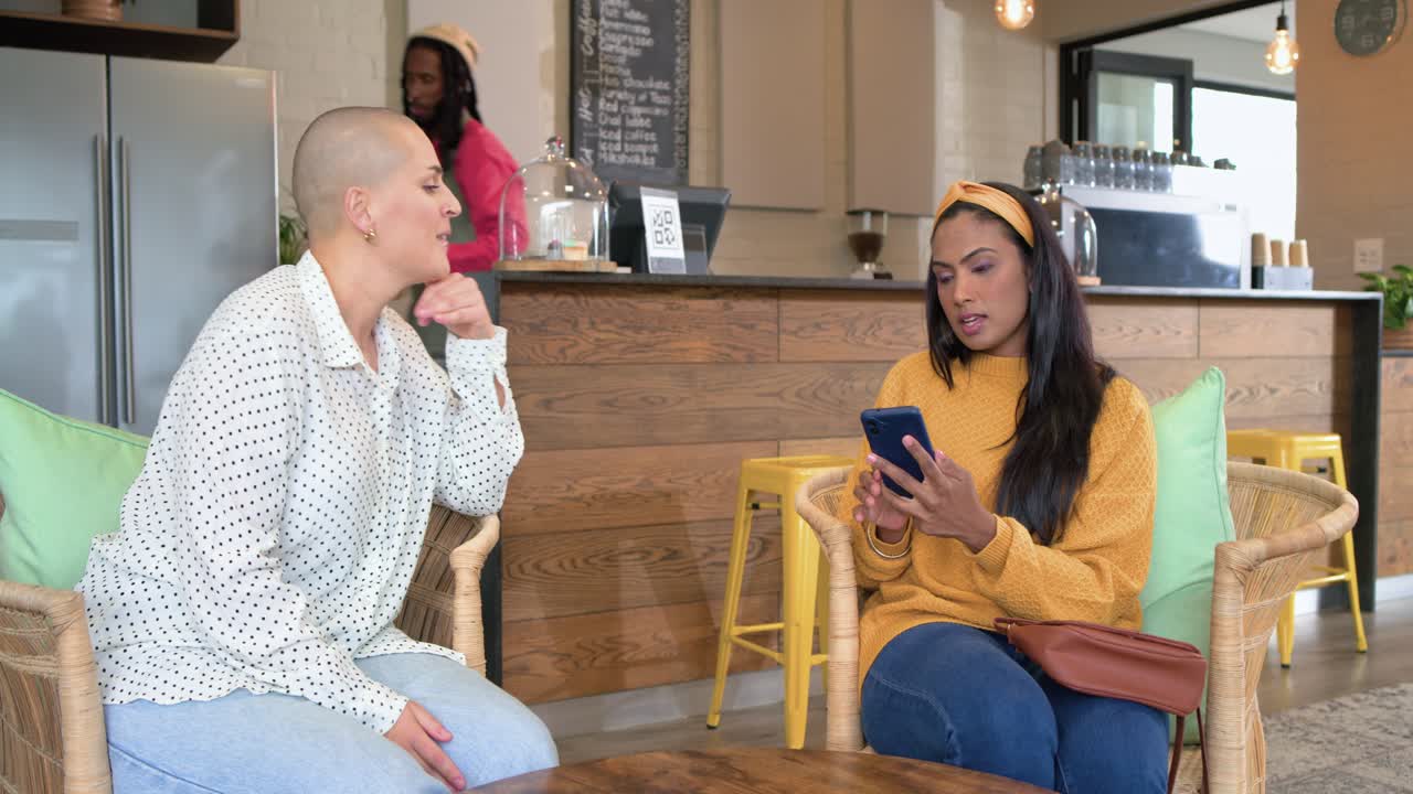 Mangfoldig gruppe kvinnelige venner som prater ved et bord og mottar kaffe fra en svart mannlig barista når bestillingen er klar.