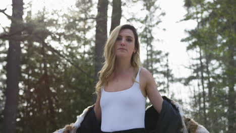 beautiful young trendy woman wearing a fur jacket posing in a winter forest setting