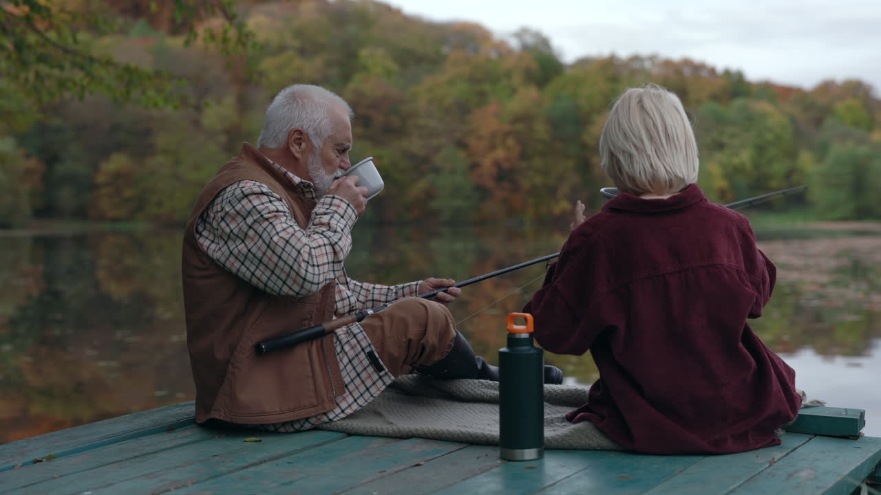 Grandfather and child fishing on a lake pier in autumn