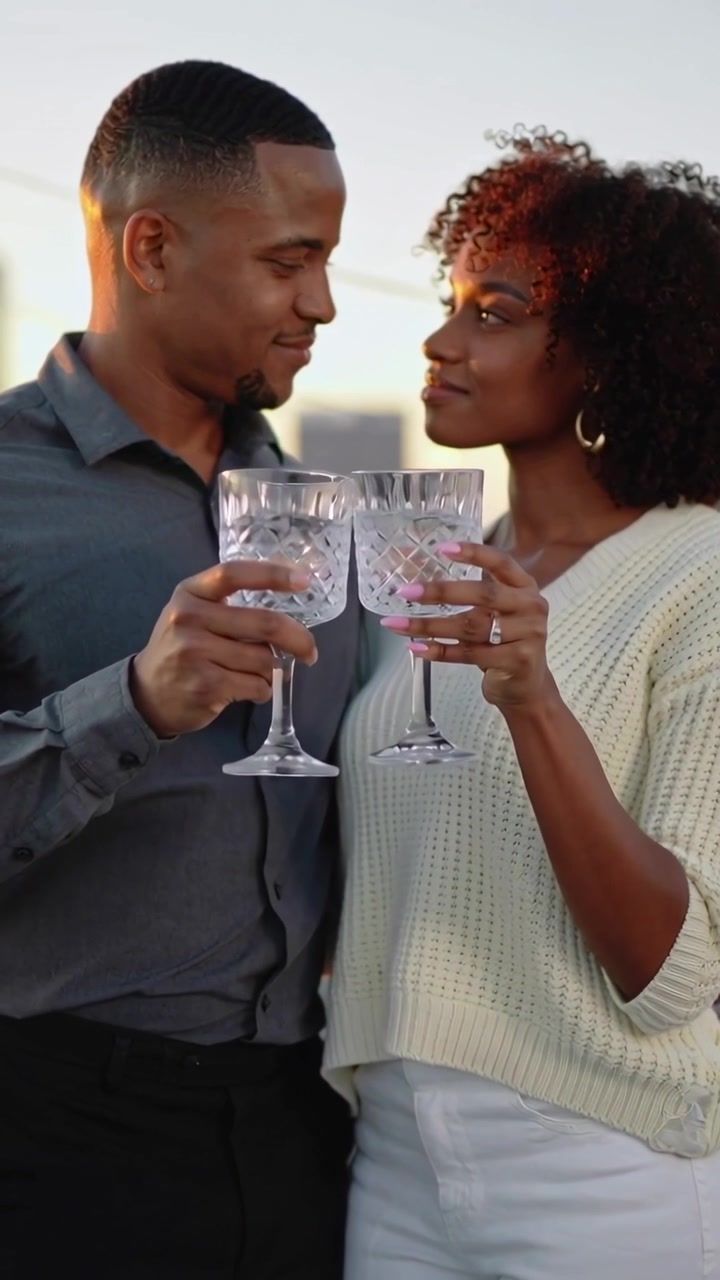 Vertical video: Sunset urging couple in sweater lifting wine goblets on roof, toasting