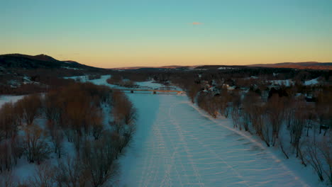 picturesque aerial view flying along a frozen snow covered river at sunset