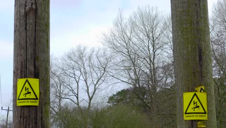 An-establishing-shot-of-high-voltage-warning-signs-mounted-on-wooden-gum-poles,-a-safety-precaution-bringing-attention-to-the-risk-and-dangers-of-the-current-carried-by-the-poles-in-Norfolk,-England