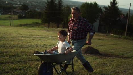 video of grandfather driving his grandson in wheelbarrows at sunset