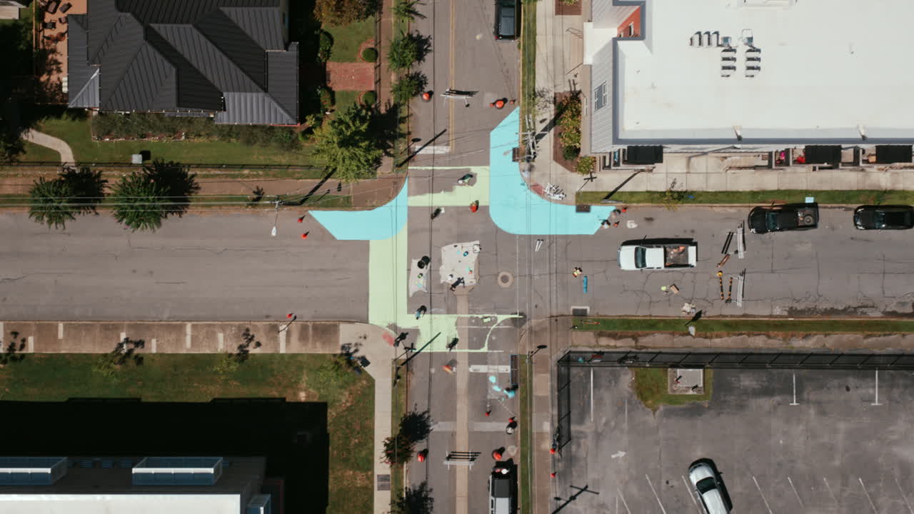 Aerial top-down view of volunteers painting a colorful intersection mural in Chattanooga, adding bright blue and green designs to the street