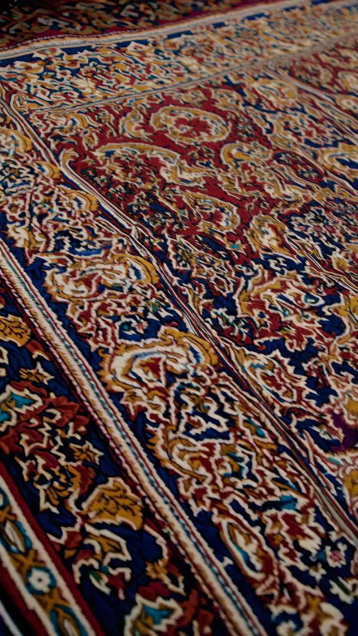 Close-up video angle of an intricate Persian rug, showcasing vibrant red, blue, and gold patterns