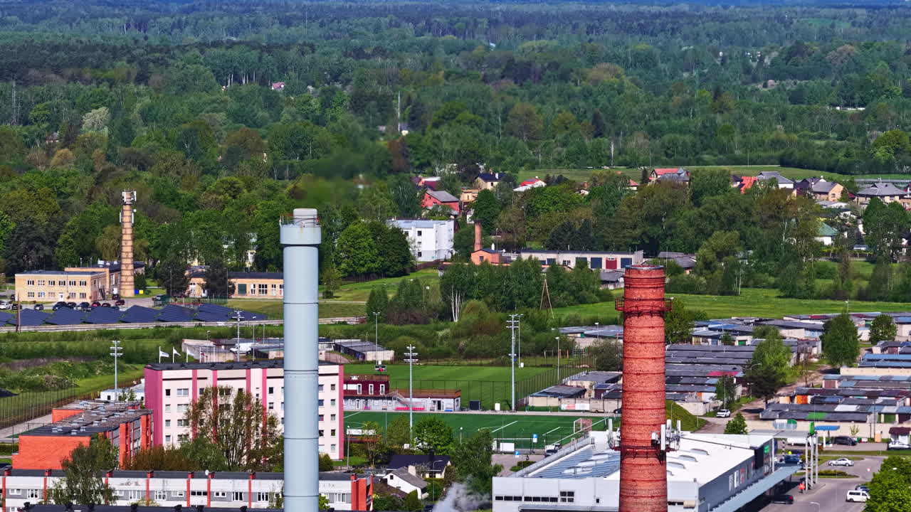 Aerial view of smoke stacks and rooftops in green urban district near forest edge