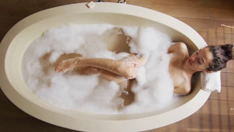 relaxed biracial woman with vitiligo lying in bathtub with foam, pampering herself