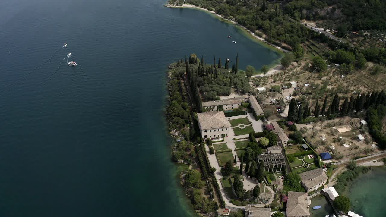Inclinazione aerea del drone da una vista a volo d'uccello a un ampio panorama a Punta San Vigilio sul Lago di Garda, che rivela acqua turchese, la costa e un suggestivo paesaggio italiano.