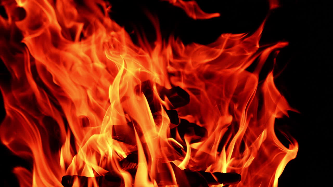 Un mucchio di ceppi di legno brucia nel falò. Vista ravvicinata delle fiamme che danzano nel vento nell'oscurità. Primo piano.