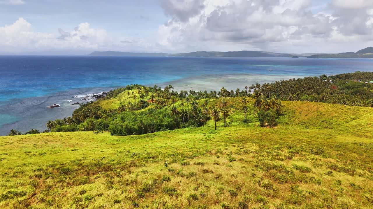 Colline verdi vivaci incontrano un mare turchese sull'isola di Corregidor, Siargao. La costa è fiancheggiata da palme e coste frastagliate, con isole distanti visibili sotto un cielo parzialmente nuvoloso.