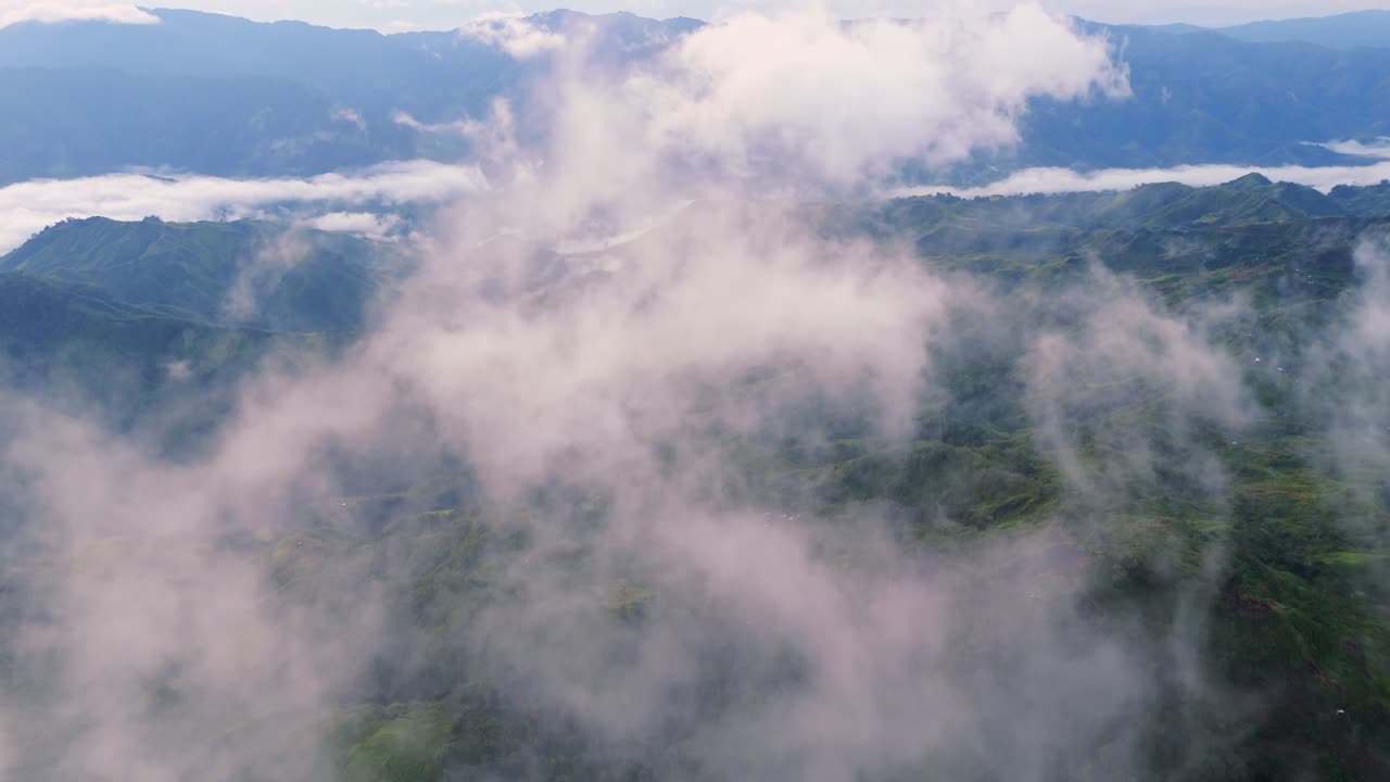 Aerial drone shot of lush green mountain ridges covered in thick white fog and clouds. Scenic morning landscape in the highlands of Davao Philippines showing the sea of clouds phenomenon