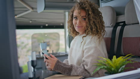 mujer sonriente sosteniendo un teléfono inteligente en la ventana del remolque de cerca. dama navegando por el teléfono