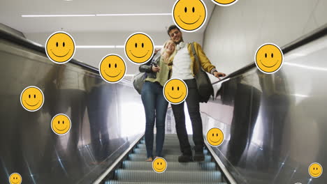 animation of digital emoji icons floating over happy caucasian couple embracing on moving stairs