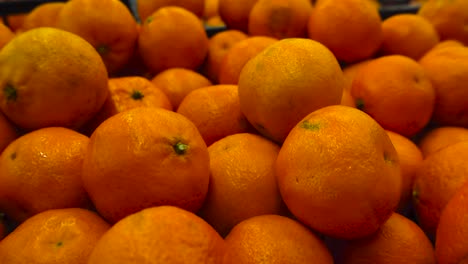 close up footage gliding over beautiful vibrant orange colored clementines or tangerines that are on top of each other in a pile. the fruit skin has texture and some fruit have spots on them.