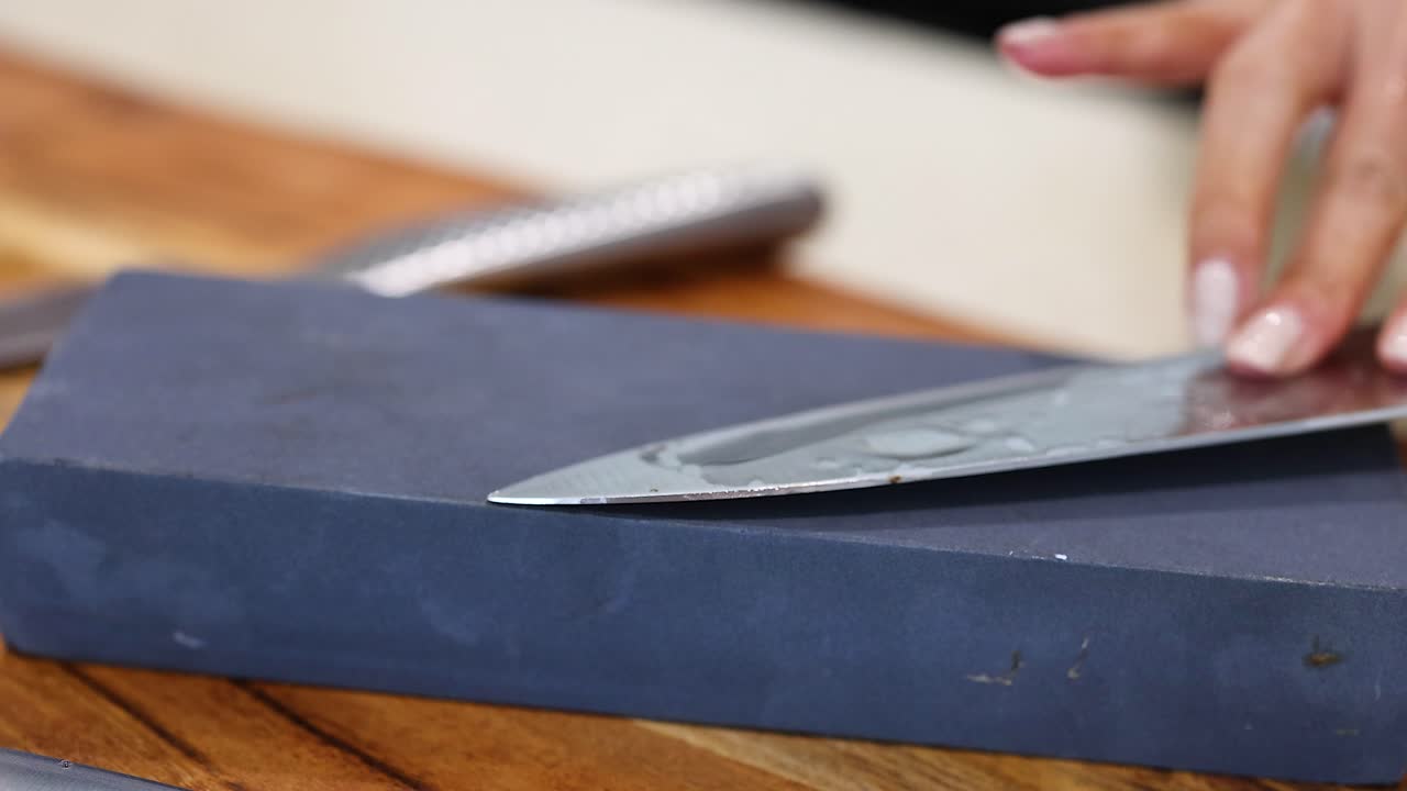 A person sharpens a knife on a stone in a well-lit kitchen, focusing on precision and technique