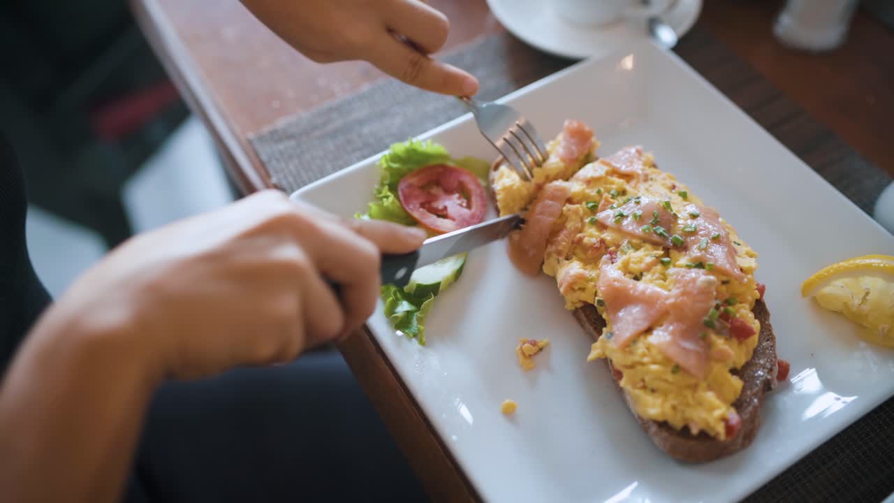 mujer cortando y comiendo un sándwich con salmón y huevos en pan tostado