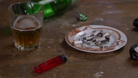 pistola de vidrio de botella de cerveza y cenicero en una mesa de madera