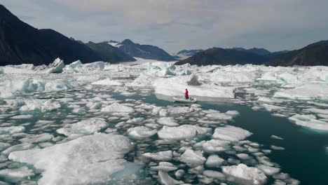 Man-Sailing-On-Lake-With-Broken-Pieces-Of-Ice-Floating-With-Snow-Capped-Mountains-In-Background-At-Glacier-Bay,-Alaska