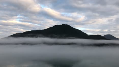 slow motion view from a ship of a dark, alaskan mountain behind the layers of the morning, ocean fog