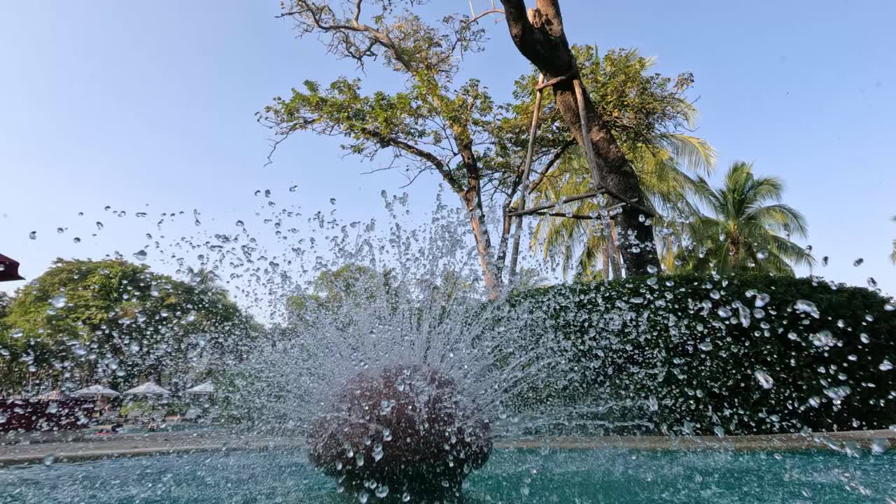 Water balloon exploding mid-air against nature backdrop.