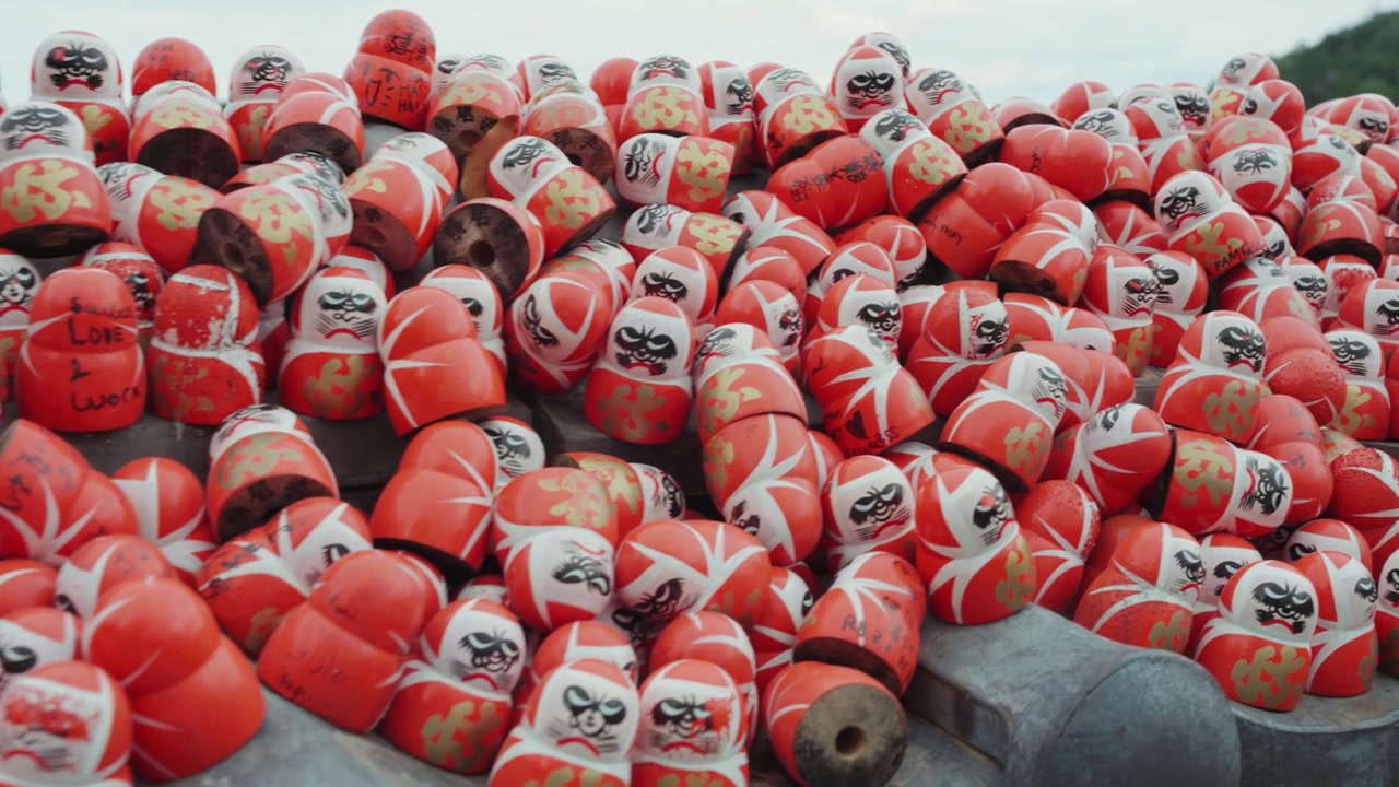 A peaceful view of red Daruma dolls at Katsuoji Temple, surrounded by lush greenery, atmospheric mist, and traditional Japanese temple architecture.