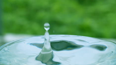 droplet of water creating ripples and small waves in a glass of water and splattering over the rim of the container