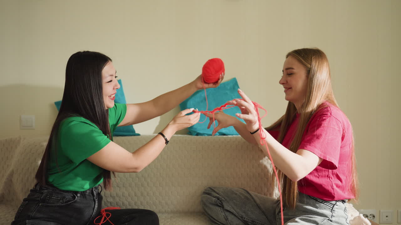 Mujeres intercambiando consejos sobre lanas y puntos, mujeres asiáticas y caucásicas practicando juntas el arte de tejer, mujeres diversas aprendiendo y compartiendo patrones de puntos con coloridas lanas en el interior.