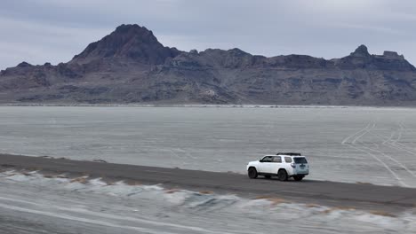 tracking drone shot of white suv vehicle moving on road in desert landscape