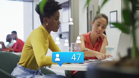 Animation-of-profile-icon-with-increasing-numbers-against-two-diverse-women-discussing-at-office