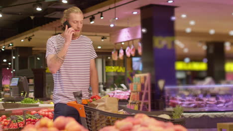 joven caucásico hablando en un teléfono inteligente en un supermercado