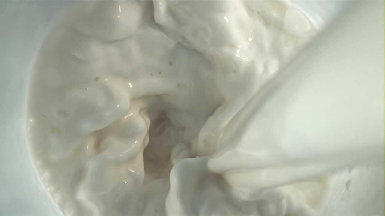Leche blanca fresca vertiéndose y salpicando en un tazón.
