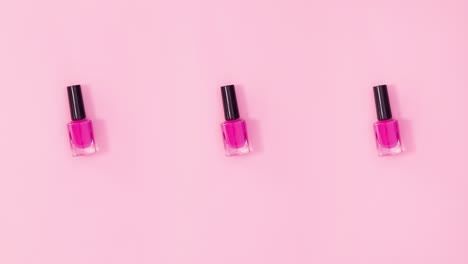 tres botellas de esmalte de uñas giran sobre un fondo rosa pastel. detenga el movimiento
