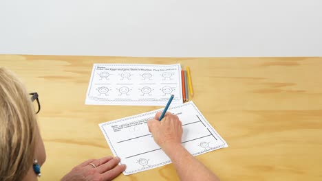 a female teacher sits and fills out a child's worksheet in anticipation for back to school in the fall