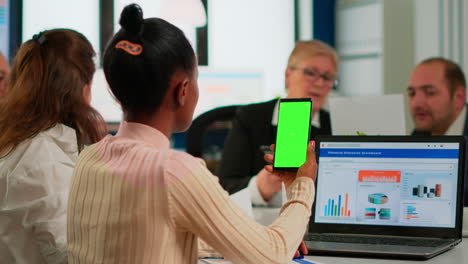 black businesswoman sitting at conference desk holding smartphone with green screen