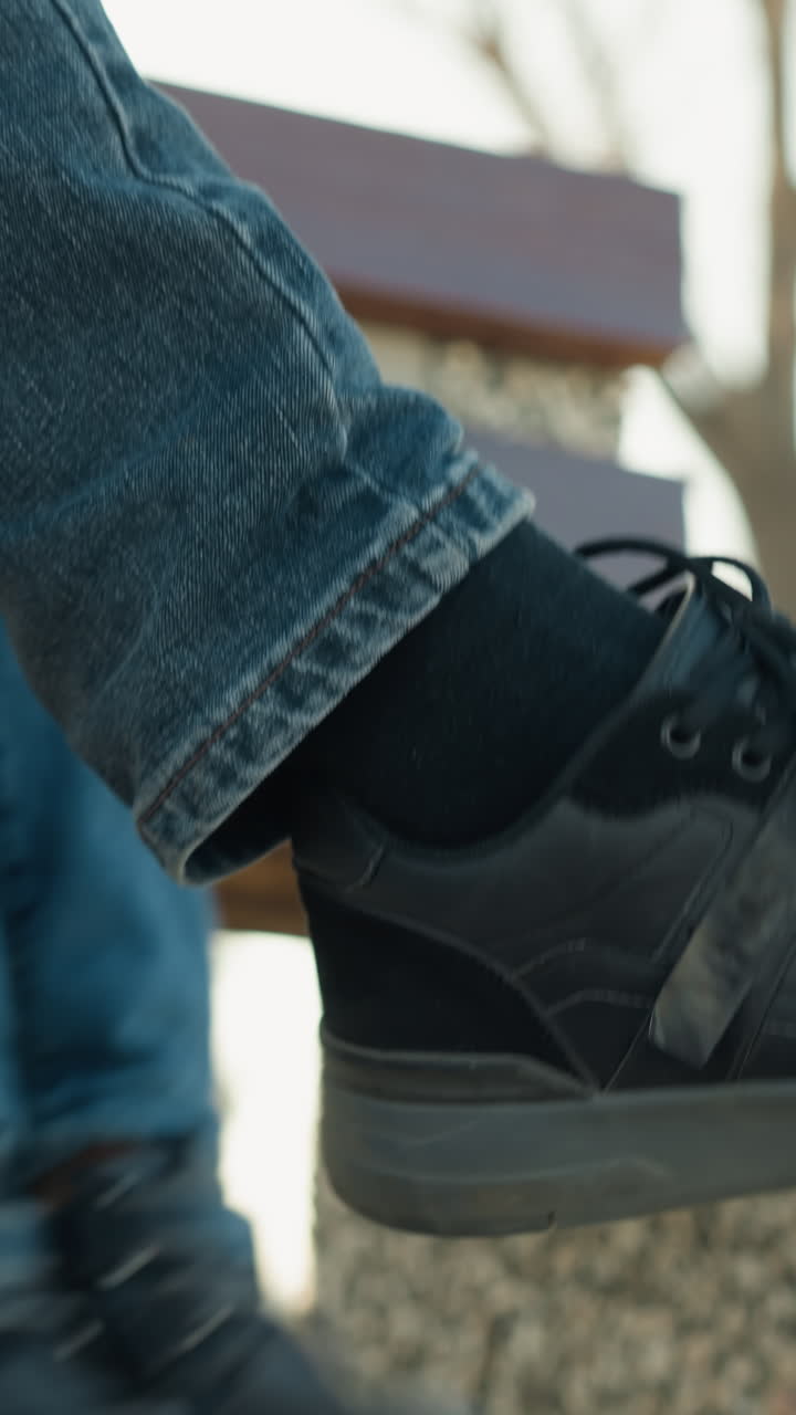 Close-up of an adult and a child sitting closely together on a bench, with the child gently hitting the adult's crossed leg, both are wearing jeans and boots, with the adult have a black socks