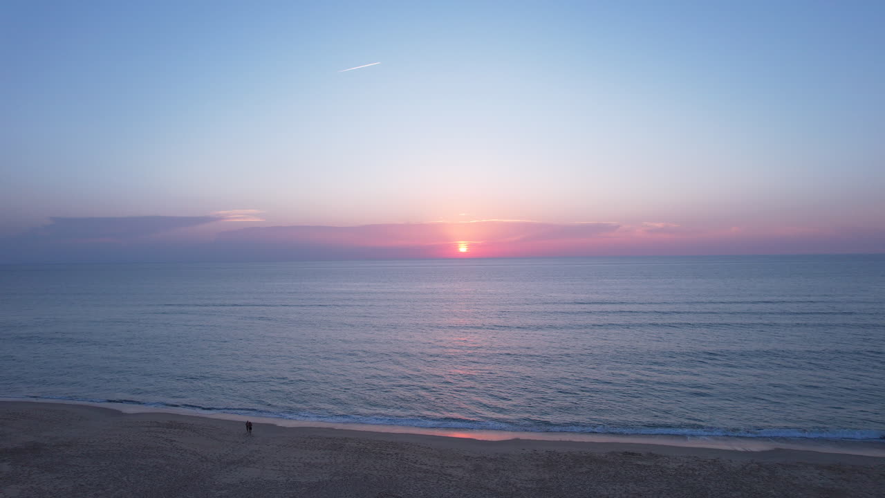 A drone shot ascending to reveal the beach and horizon at sunset, gradually disappearing the beach and showcasing the vast ocean. The warm colors of the sunset create a serene atmosphere.