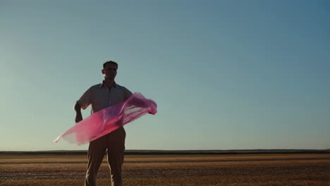 man in a field holding a pink scarf